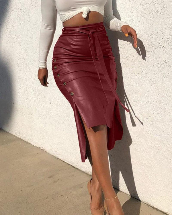femme en talons portant une jupe midi asymétrique plus longue derrière que devant en simili cuir rouge ceinturé avec une fente et des boutons pressions sur le côté