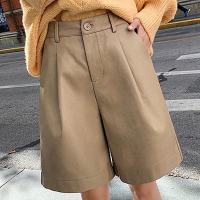 Jeune femme dont on voit uniquement le haut des jambes, porte un pull orange et un short beige à coupe classique avec poche et long