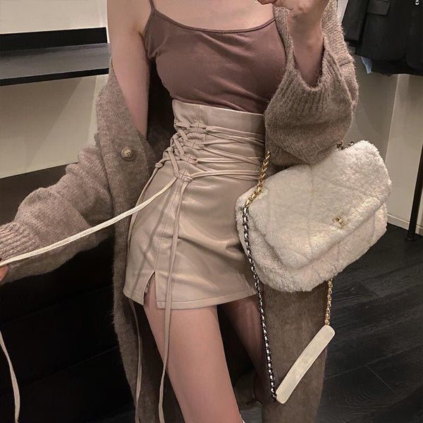 femme portant un long gilet et un sac beige avec une mini jupe en simili cuir beige fendue avec de longs lacets qui resserrent la jupe