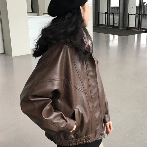 Une femme portant un manteau oversize marron en simili cuir, elle est brune et a une main dans la poche