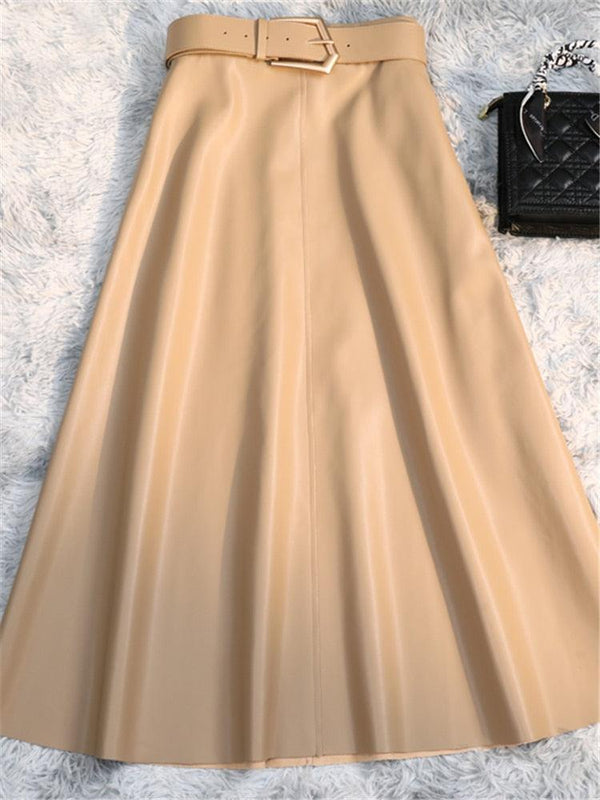 Une jupe longue mi mollet en simili cuir beige avec une ceinture avec une boucle dorée posée au sol