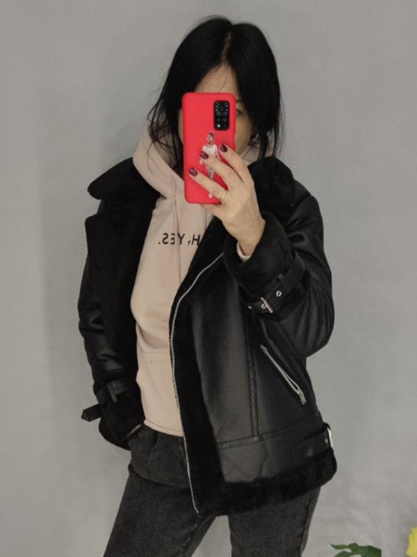 Une femme en train de seprendre en selfie  qui porte un blouson en simili cuir noir, son téléphone a une coque rouge.